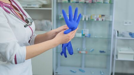 Young women Caucasian doctor in white medical coat and violet stethoscope inflates a rubber blue glove to check if it is leaky and can be usedの写真素材