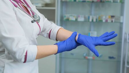 Young Caucasian nurce in white medical coat and violet stethoscope looking and check a rubber blue gloves to if it is leaky and can be used. Side viewの写真素材