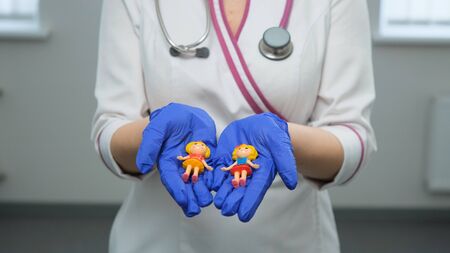 Caucasian young women medic holds toy figures of childrenand close to her heart on a white background. Children protection, love and care concept. Front view. Medium shot.の写真素材