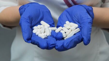 Young women doctor in white medical coat and rubber blue gloves holds a lot of white pills tablets in the palm of her hands. Concept of Health, Drugs, Contraception, Choiceの写真素材