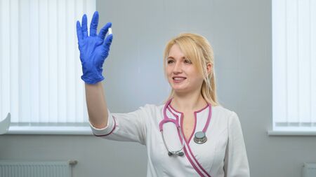 Caucasian young attractive female scientist doctor in white medical coat, violet stethoscope holding a white pill with fingers in blue gloves in the pharmaceutical research laboratoryの写真素材
