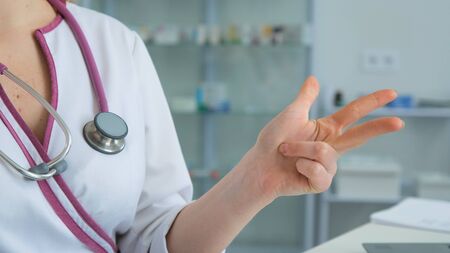 Clouse up of Medical Staff Hospital woman doctor gestures with his hand and counts with her fingers in the clinic in a white coat sittingの写真素材