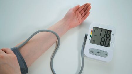 Woman measures his blood pressure at the table. Modern automatic white and grey tonometer displaying on monitor the numbers of measurementの写真素材