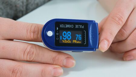 Woman holding in her hands blue Pulse Oximeter. Monitor showing saturation of oxygen in the blood and pulse rate of patient. Close upの写真素材