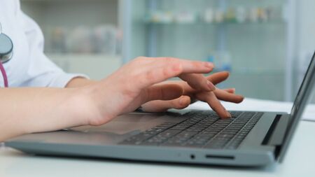 Close up shot of doctors hands, who is dressed in a white robe. The woman prints text on the keyboard of a portable laptopの写真素材