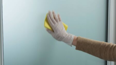 Hand in white gloves cleaning window with yellow rag and cleanser spray at home or office.の写真素材