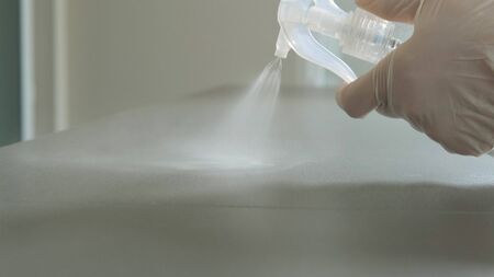 Hands in medical white gloves sprays disinfectant and wipe the surface with a yellow rag.の写真素材