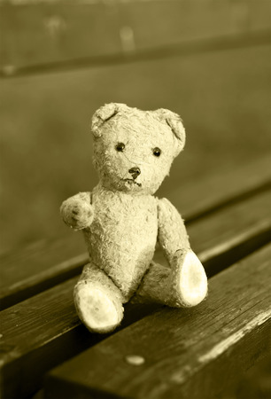 Toy bear sitting on a bench and giving his paw for helpの写真素材