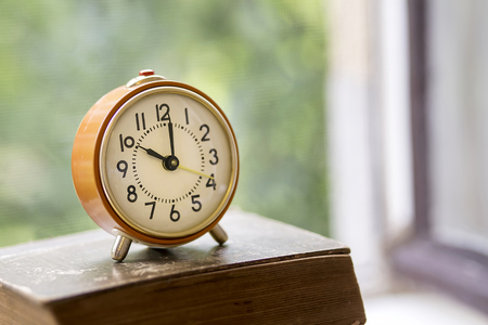 Retro alarm clock on an old book in the windowの写真素材