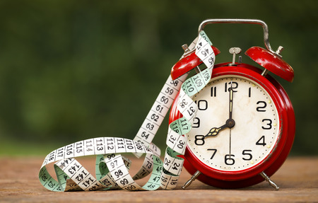 Daylight savings concept - web banner of a red alarm clock and tape measure with blank, copy spaceの写真素材