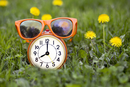 Summertime concept - orange sunglasses and retro alarm clock in the grass with yellow flowers