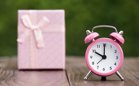 Time to gift, shopping concept, pink alarm clock with a gift box in the background