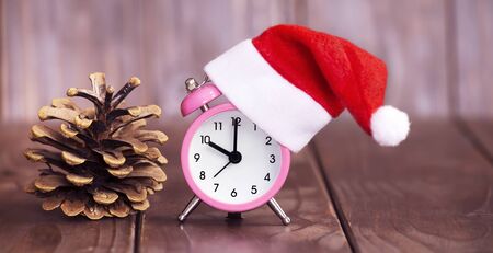 Time to gift concept, pink santa alarm clock and pine tree cone on wooden background, web bannerの写真素材