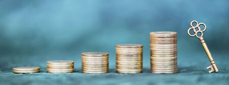 Money savings, gold coins and key on blue background. Coronavirus financial stimulus, aid package, help symbol. Web banner, copy space.の写真素材