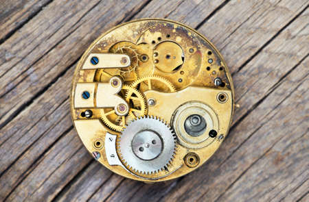 Antique metal pocket watch clockwork with gears on wooden background