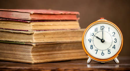 Old retro alarm clock and books on the table, back to school, education, learning history banner