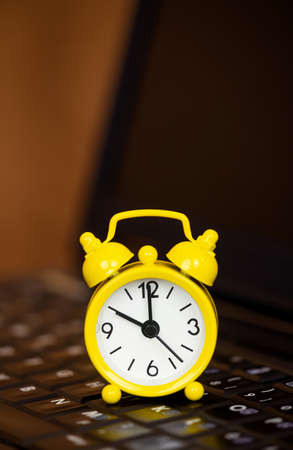 Yellow clock on a black computer laptop, business time management, success background
