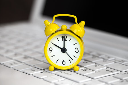 Yellow alarm clock on a white laptop, daylight savings time background