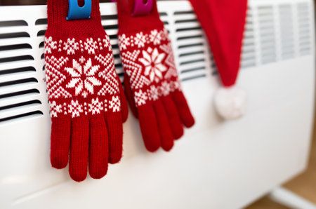 Red christmas gloves and santa hat on a warm heater radiator in a cold winter day at home. Christmas clothes.の写真素材