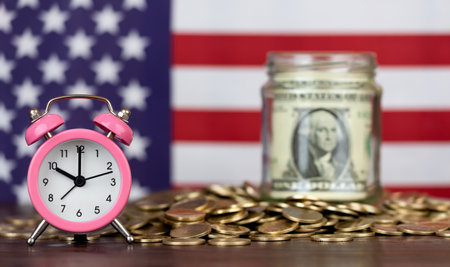 Alarm clock with gold money coins and dollar bill with American flag in the background. Retirement savings, financial planning concept.の写真素材
