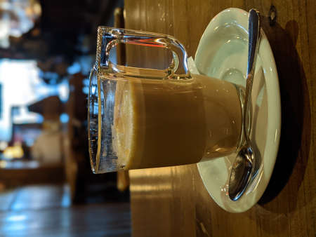 A cup of coffee on a wooden table and a teaspoon on top of the cup plateの写真素材