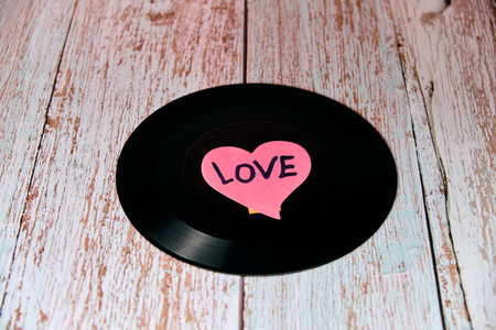 Black vinyl record with a heart in the center on a wooden table.