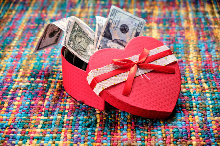 Gift in the shape of an open heart and inside full of dollars, on a table with many colors. Happy Valentine's Day, Mother's Day, birthday gift.の写真素材