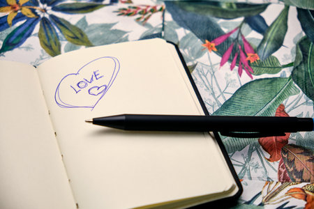 Open notebook with a pen and written the word Love, on top of a table with a tropical pattern.の写真素材