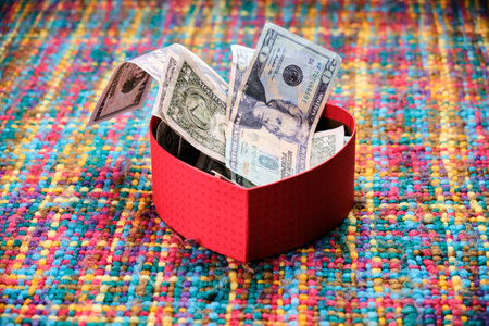 Gift in the shape of an open heart and inside full of dollars, on a table with many colors. Happy Valentine's Day, Mother's Day, birthday gift.の写真素材