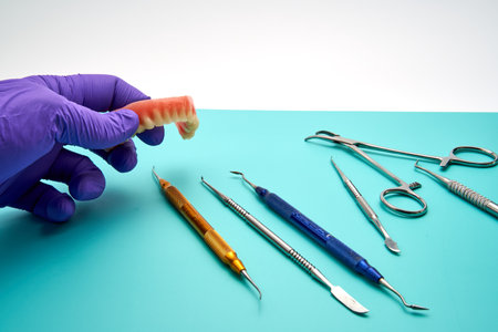 A dental technician picks up a denture from a workbench with various dental prosthetic tools.