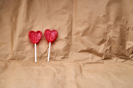 Two red heart-shaped lollipops together representing love, on a cardboard textured background.の写真素材