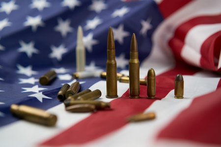 Closeup of cartridges and bullets of different sizes arranged on top of American flag with stars and...
