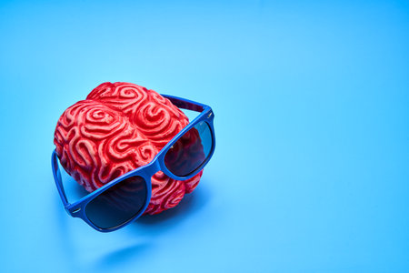 Red plastic human brain wearing blue sunglasses on a blue background.