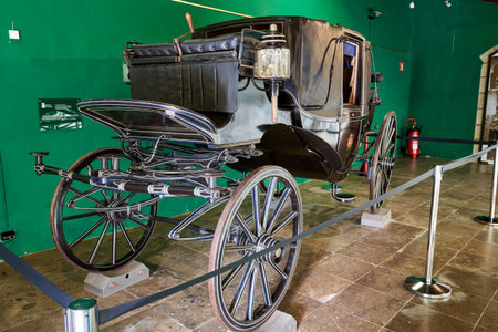 An antique carriage is behind a fence in a museum