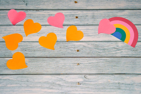 Paper hearts along with rainbow placed on wooden surface