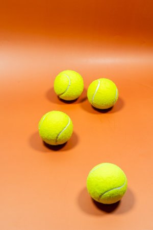 Four bright yellow tennis balls on an orange surface.の写真素材