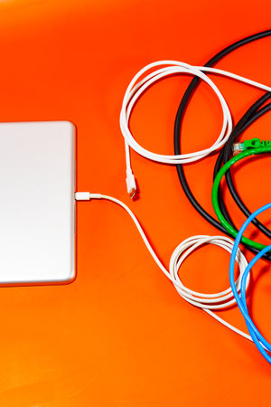 Composition of various cables and device on orange table