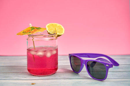 Refreshing pink drink with an umbrella and a slice of lemon and purple sunglasses.
