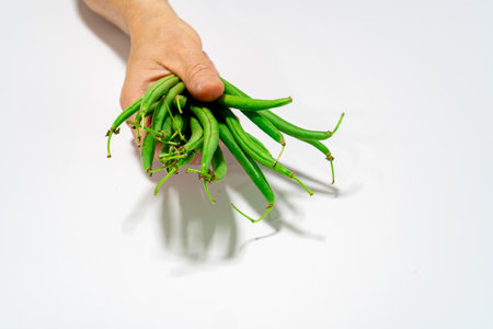 Close-up of a hand holding a bundle of fresh green beans on a white background.の写真素材