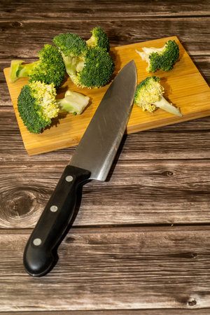 Fresh broccoli florets prepared on a wooden board with a chefs knife ready for cooking.の写真素材