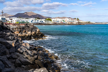 Picturesque view of a coastal town in Lanzarote, showing the sea meeting the rocky shore under a blue sky.の写真素材
