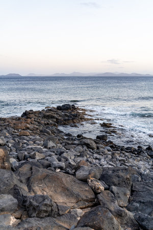 A serene coastal scene in Lanzarote showcases rocky shores and calm ocean waters at sunset.