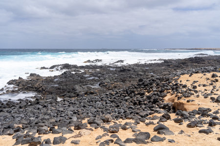 The rugged volcanic coastline of La Graciosa, with waves crashing on the shore under a cloudy sky.