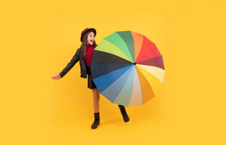 happy teen girl in hat and leather clothes having fun with rainbow umbrella, autumn mood