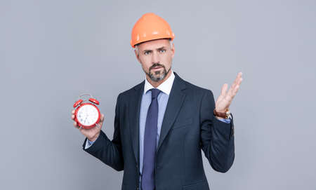 architect man in businesslike suit and hardhat holding alarm clock, time managementの写真素材