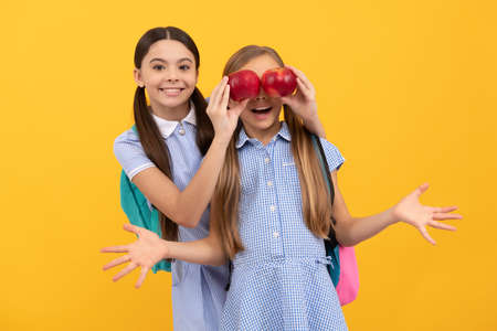 Happy child cover classmates eyes with apples yellow background, eye health