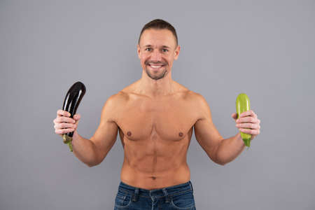 Happy muscular man hold healthy fresh vegetables grey background, mens health and erection.の写真素材