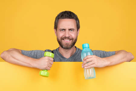happy bearded man behind paper hold fitness barbell and water bottle for spot training, health.の写真素材