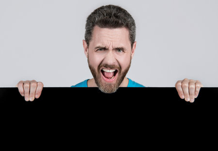 shouting bearded man behind blank black paper banner with copy space for advert, promotionの写真素材