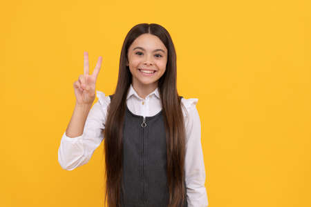 Happy girl child smile showing V sign hand gesture yellow background, peaceの写真素材